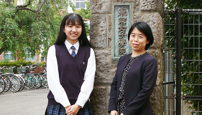 female student with female teacher standing infront of school